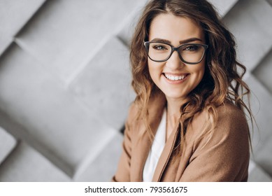 Portrait of a beautiful charismatic girl with a charming smile in glasses, which sits against a gray wall