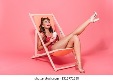 Portrait of a beautiful cheerful pin-up woman wearing swimsuit relaxing on a hammock isolated over pink background
