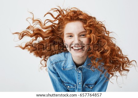 Portrait of beautiful cheerful redhead girl with flying curly hair smiling laughing looking at camera over white background.