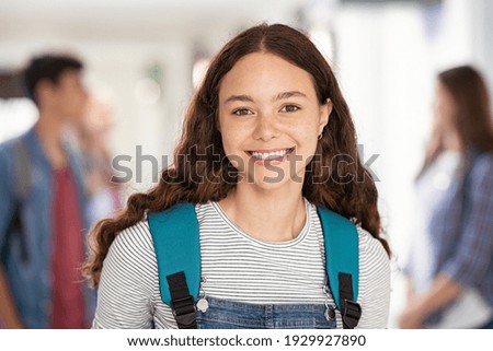 Portrait of beautiful college student standing in hallway school while looking at camera. Intelligent university girl with backpack smiling. Proud and satisfied teen in high school corridor standing.
