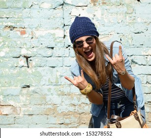 Portrait Of Beautiful Cool Girl Gesturing In Hat And Sunglasses Over Grunge Wall