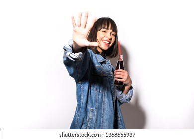 Portrait Of Beautiful Crazy Smiling Brunette Woman Girl In Casual Jeans Jacket With Stop Gesture On White Drinking Soda From Bottle With Straw