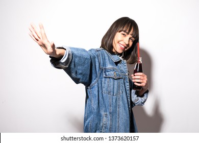 Portrait Of Beautiful Crazy Smiling Brunette Woman Girl In Casual Jeans Jacket With Stop Gesture On White Drinking Soda From Bottle With Straw