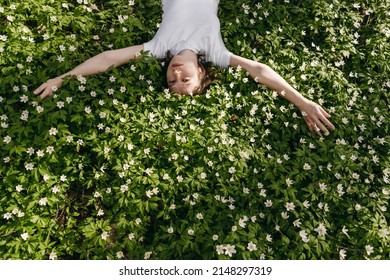 The Portrait Of Beautiful Cute Woman No Makeup In White Shirt Laying Down On Green Grass With White Flowers. Sunny Summer Day, Wild Nature, Mood Vacation, Relax. Top View Of Girl. Be Free, Love Forest