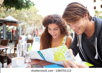 Portrait Of Beautiful Diverse Young Tourist Couple Relaxing In Coffee Shop Exterior Reading Street Map, Outdoors. People Discovery City Break Trip, Travel Holiday, Leisure Recreation Active Lifestyle.