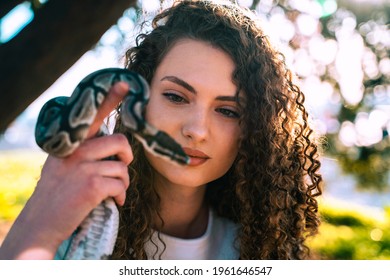 Portrait of beautiful eastern european young woman holding a snake. Outdoor portrait in front of the huge tree. 