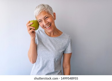 Portrait of a beautiful elderly woman holding an apple, smiling, isolated on gray background. Happy Woman Holding Granny Smith Apple. An aple a day keeps doctor away - Powered by Shutterstock