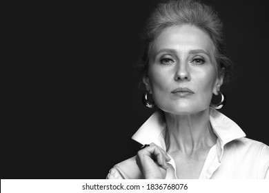 Portrait Of A Beautiful Elderly Woman In A White Shirt With Classic Makeup And Gray Hair. Black And White Photo