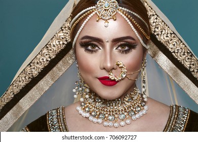 Portrait of a Beautiful Elegant Female Indian Model in Traditional Ethnic Asian Bridal Costume with Makeup and Heavy Jewellery in studio blue background