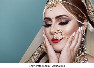Portrait of a Beautiful Elegant Female Indian Model in Traditional Ethnic Asian Bridal Costume with Makeup and Heavy Jewellery in studio blue background