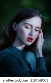 Portrait Of A Beautiful Fairy Tale Girl With Dark Wavy Hair, Standing In A Green Dress In A Dark Forest. Sunlight Falls On Her Face. Fantasy, The Heroine Of A Fairy Tale.