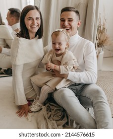 The Portrait Of Beautiful Family Of Mother, Father, Daughter In White Clothes Near Mirror At Home. Nice Modern Minimal Interior. Beige Colours. Happy People, Studio Photoshoot, Hugging.