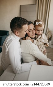 The Portrait Of Beautiful Family Of Mother, Father, Daughter In White Clothes Near Mirror At Home. Nice Modern Minimal Interior. Beige Colours. Happy People, Studio Photoshoot, Hugging.