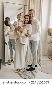 The Portrait Of Beautiful Family Of Mother, Father, Daughter In White Clothes Near Mirror At Home. Nice Modern Minimal Interior. Beige Colours. Happy People, Studio Photoshoot, Hugging.