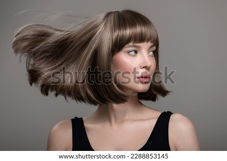 Portrait of beautiful fashion woman with bob hairstyle. Flying hairs up. Gray background