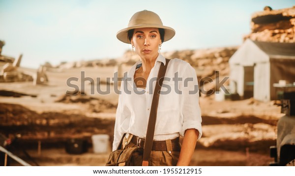 Portrait of Beautiful Female Adventurer Posing\
and Looking at Camera. Stylish Great Archaeologist Standing with\
Ancient Civilization, Fossil Remains Archeological Site, Forgotten\
City in Background