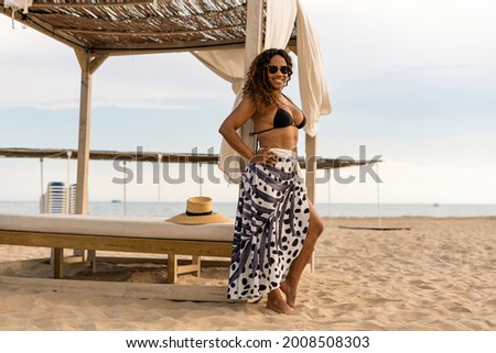 Portrait of beautiful female in bikini and pareo looking to the camera enjoying summer vacation trip on the beach.