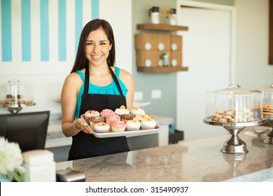 Portrait of a beautiful female business owner showing some of her freshly baked cupcakes and smiling - Powered by Shutterstock