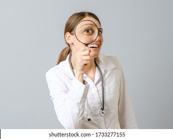 Portrait of beautiful female doctor looking through loupe isolated on gray background - Powered by Shutterstock