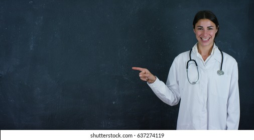 Portrait of a beautiful female doctor (student) stands by a black board, on a black background. Concept: ideas, school, university, chemistry, science, teachers, memory, biology, physician, college.