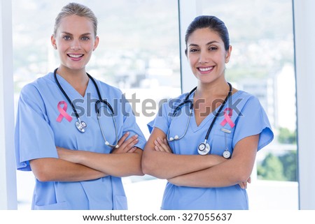 Portrait of beautiful female doctors against pink breast cancer awareness ribbon
