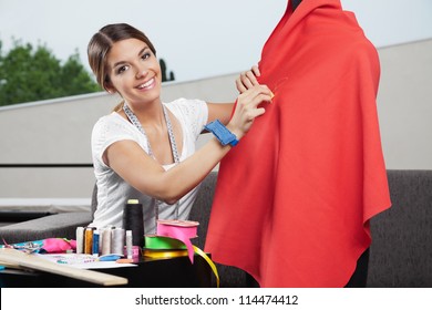 Portrait of beautiful female fashion designer working on  red fabric with dressmaking accessories on table - Powered by Shutterstock