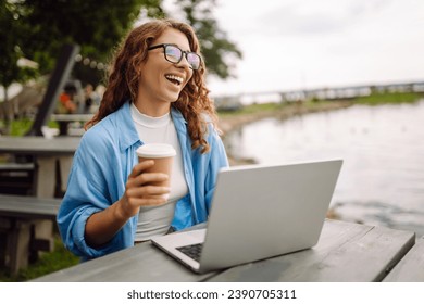 Portrait of a beautiful female freelancer working online using a laptop and enjoying the natural landscape overlooking the lake. Freelance concept, nature.