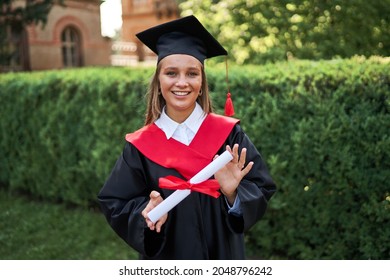 Portrait of beautiful female graduate in graduation gowm with diploma looking at camera. - Shutterstock ID 2048796242