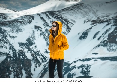 Portrait of a Beautiful Female Hiker in Orange Jacket Exploring the Mountains on a Sunny Day. Woman puts the hood of her jacket on while standing on the summit of a scenic mountain - Powered by Shutterstock