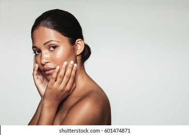 Portrait of beautiful female model with hands on her face looking at camera. Young woman with clean and healthy skin posing against grey background.