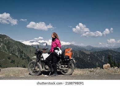 Portrait of beautiful female motorcyclist sitting on motorcycle on top of mountain. Dangerous mountain road in moto trip