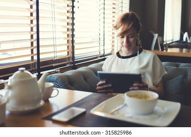 Portrait of beautiful female student listen or studying on-line training course in headphones while using her digital tablet charming young woman have video conversation while breakfast in coffee shop