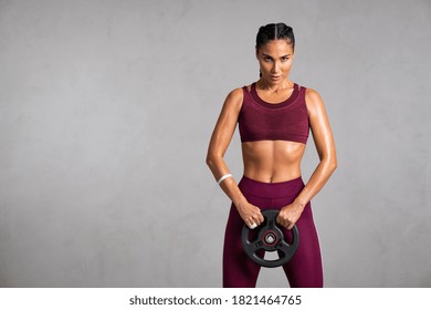 Portrait of beautiful fit woman exercising with a weight plate. Determined sportswoman lifting heavy weight dumbbell isolated on gray background.  - Powered by Shutterstock