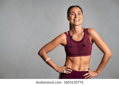Portrait of beautiful fitness woman smiling and looking at camera isolated on grey background. Mid woman in sportswear relaxing after training at gym. Happy fit girl on gray wall with copy space.