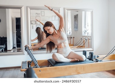 Portrait of beautiful fit-shape female dressed sporty doing stretching exercises using pilates reformer machine in sport athletic gym. Active people training or medical rehabilitation concept image - Powered by Shutterstock