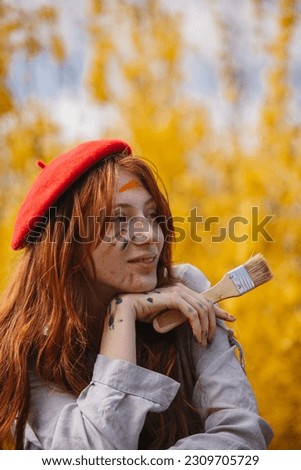 Portrait of beautiful ginger girl painter posing with her big brush while looking away