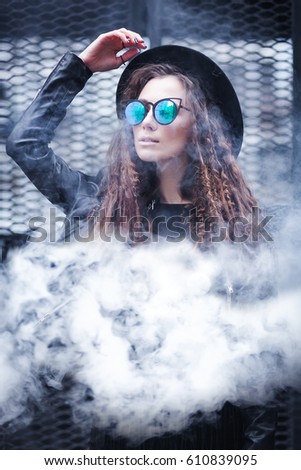 Portrait of a beautiful girl in black hat and sunglasses in a cloud of smoke
