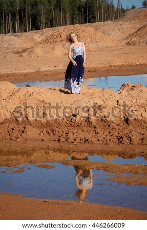 Portrait of a beautiful girl in a blue dress on the sand near the water