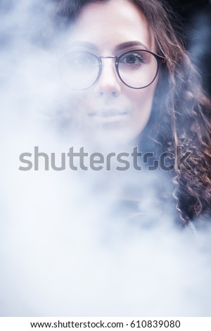 Portrait of a beautiful girl with brown eyes in glasses in a cloud of smoke looking in camera. The girl is like Harry Potter