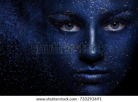 Portrait of a beautiful girl closeup. Face painted blue paint. The effect of the collapse. flying powder particles. The concept of space