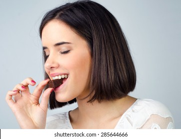 Portrait of the beautiful girl eating chocolate cookies isolated on gray background.