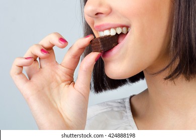 Portrait of the beautiful girl eating chocolate cookies isolated on gray background.