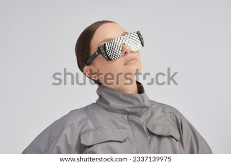 Portrait of a beautiful girl fashion model posing with back in a stylish grey jacket and mirrored sunglasses on a grey studio background. Futuristic Fashion style. High fashion.