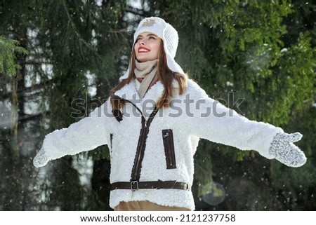 Portrait of a beautiful girl in fashionable sheepskin coat and knitted hat walking joyfully in the park and enjoying a sunny winter day. Winter fashion. 