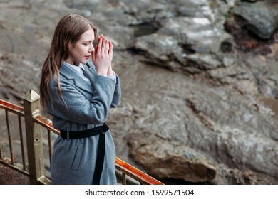 Portrait Of A Beautiful Girl In A Gray Coat On A Gray Background Of A Mountain River. Copy Space