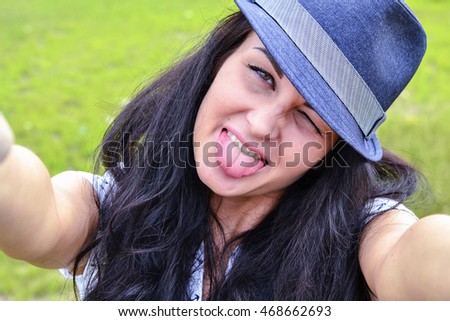 Portrait of beautiful girl in hat on the background of grass and sun. Girl teases and shows language