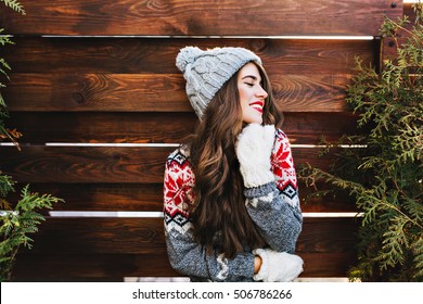 Portrait beautiful girl with long hair and red lips in warm winter clothes on wooden background. She is smiling to side and keeps eyes closed - Powered by Shutterstock