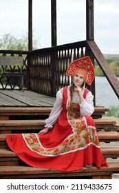 Portrait of a beautiful girl in a national Russian costume with a kokoshnik on her head.A Russian girl in a traditional red sundress, white shirt and crown.Blonde with a long braid.Folk, retro, ethno.