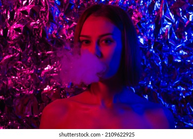 Portrait beautiful girl in neon light purple  pink   blue  A young woman in futuristic image blowing smoke from her mouth  Girl smoking hookah