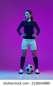 Portrait Of Beautiful Girl, Professional Female Soccer Player With Football Ball Isolated On Purple Background In Neon. Concept Of Sport, Fitness. Young Spotive Girl In Black And White Football Kit